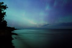 an aurora bore is seen in the sky above water and trees on the shore at night