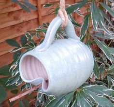 a blue bird feeder hanging from a tree in front of a wooden fence with green leaves