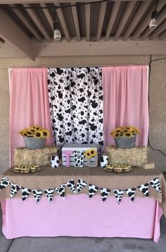 a table topped with hay bales covered in fake flowers and sunflowers next to a pink curtain