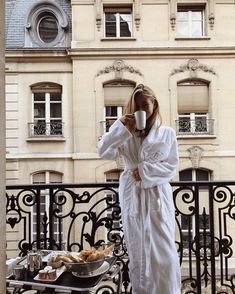 a woman in a bathrobe holding a cup of coffee while standing on a balcony