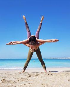 two women doing handstands on the beach in front of blue sky and water