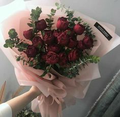 a bouquet of red roses wrapped in pink tissue paper with greenery on the side