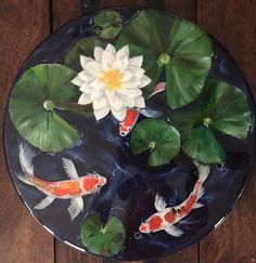 a glass plate with water lilies and koi fish in it on a wooden table