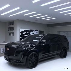 a black suv is parked in a showroom with white walls and ceiling lights above it