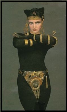 a woman dressed in black and gold with her hands on her hips