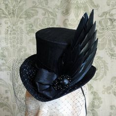 Simple yet full of impact,The Nevermore,this gothic mini top hat is utterly suitable for the darkest of appearances. Covered with black silk shantung, it is gracefully embraced with matching black band around the crown.It is elegantly embellished with a black feather, faux raven wing, Gothic Hat For Halloween, Black Gothic Mini Hats For Costume Party, Gothic Black Brimmed Costume Hat, Gothic Hat For Halloween And Alternative Fashion, Gothic Halloween Hat For Alternative Fashion, Black Gothic Hat For Costume, Gothic Top Hat With Short Brim For Halloween, Gothic Black Top Hat For Costume Party, Black Gothic Top Hat For Costume Party