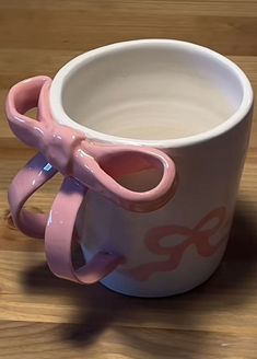 a pink and white coffee cup sitting on top of a wooden table next to a pair of scissors