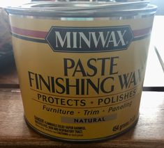 a can of paste finishing wax sitting on top of a wooden table next to a window