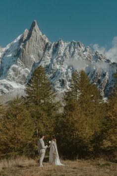 a bride and groom holding hands in front of a snowy mountain range with pine trees