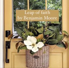 a basket filled with flowers sitting in front of a yellow door that says leap of faith by benamin moore