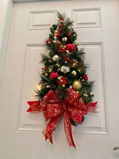 a decorated christmas tree hanging on the front door with red and gold ornaments around it