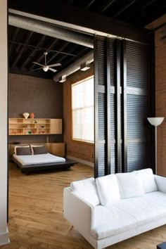 a living room filled with white furniture next to a wooden floor and wall covered in windows