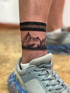 a man's foot with a mountain scene tattoo on the side of his leg