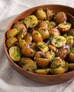 a wooden bowl filled with potatoes covered in herbs and garnished with purple flowers