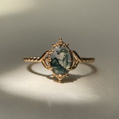 a gold ring with a green and white stone in the center on a white surface