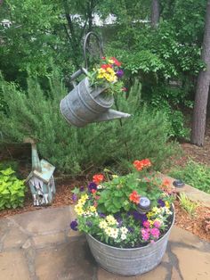 an old watering can is used as a planter for colorful flowers in the garden