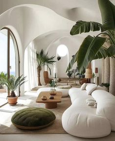 a living room filled with lots of white furniture and large potted plants on the wall