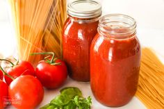 tomatoes, pasta and spaghetti on a white table with two jars filled with tomato sauce