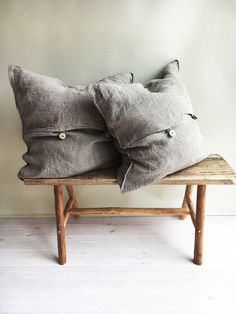 two gray pillows sitting on top of a wooden bench next to a white wall and floor