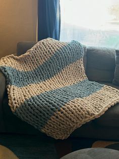 a blue and white knitted blanket sitting on top of a couch next to a window