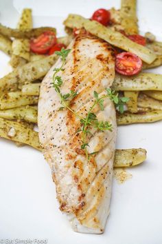 a white plate topped with chicken and french fries next to tomatoes on top of green beans