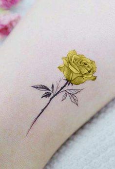 a small yellow rose tattoo on the right side of the arm, with pink flowers in the background