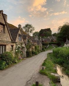 an old stone house with flowers growing on it's roof and the road leading up to it