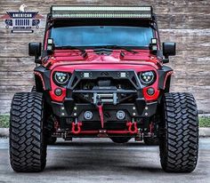 the front end of a red jeep with its lights on and four wheel drive tires