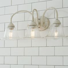 three light bathroom fixture with glass shades on white brick wallpapered walls and tile flooring