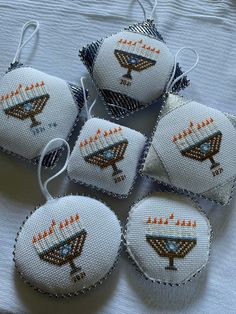 six embroidered ornaments are sitting on a white sheet, each with an orange and blue design