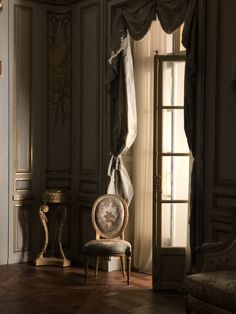 a chair sitting in the middle of a room next to a window with drapes on it