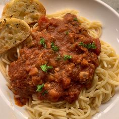 a white plate topped with pasta and meat sauce next to garlic bread on top of a table