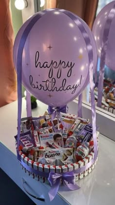 a purple balloon with the words happy birthday on it sitting in a basket filled with candy