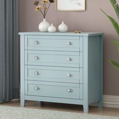 a blue chest of drawers with three vases on top and one plant in the corner