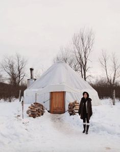 a woman standing outside of a yurt in the snow