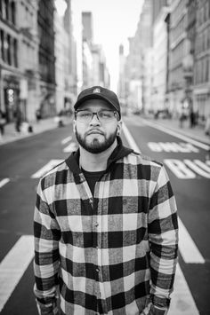 a man standing in the middle of an empty street wearing glasses and a plaid shirt