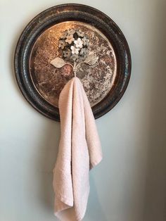 a towel hanging on the wall next to a metal bowl with flowers in it and two white towels