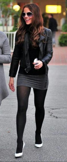 a woman walking down the street in tights and black clothing with her hand on her hip