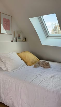 an unmade bed with white sheets and yellow pillows in a loft space under a slanted skylight