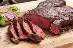 the steak is sliced and ready to be served on the cutting board with onions, celery, and pickles