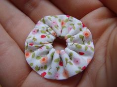 a small white flowered hair scrunch in someone's hand with pink and green flowers on it