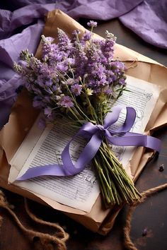 a bouquet of flowers sitting on top of an open book with a purple ribbon tied around it