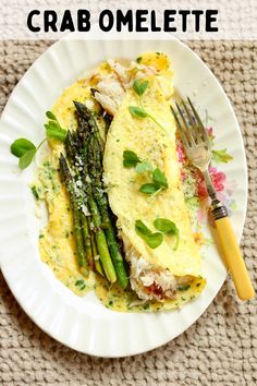 an omelet and asparagus on a white plate with a yellow fork