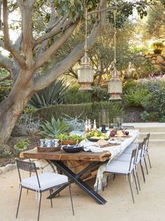 an outdoor dining table set up with chairs and plates on it, surrounded by trees