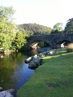 a stone bridge over a river next to a lush green field