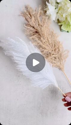 someone is holding a feather wand with white feathers and flowers in the background on a table