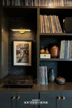 a book shelf filled with lots of books next to a wall mounted record player on top of a wooden cabinet