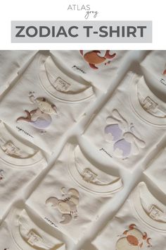 A collection of baby sweaters in cream tones, each embroidered with whimsical zodiac-themed characters, including Pisces fish, Gemini twins, and Capricorn goat-mermaid hybrids.