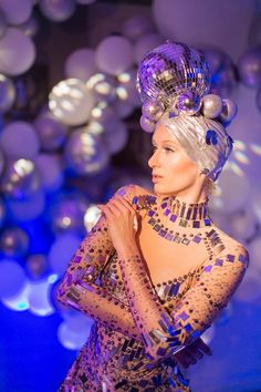 a woman in a dress and headdress is posing for the camera with balloons behind her