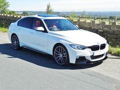 the white car is parked on the side of the road in front of a stone wall